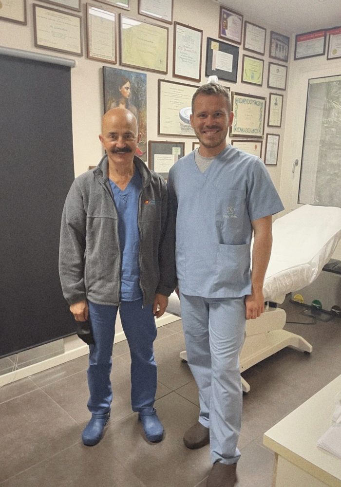 Two plastic surgeons, Dr. Žygimantas Mačys and Dr. Giovanni Botti, in surgical attire inside an advanced operating room at Villa Bella Clinic